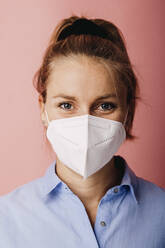Mid adult businesswoman wearing protective face mask standing against colored background - DAWF01784