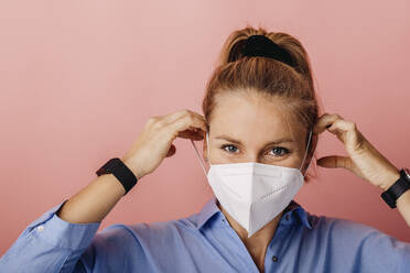 Businesswoman wearing protective FFP2 face mask while standing against colored background - DAWF01787