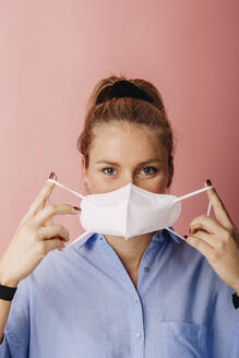 Mid adult businesswoman wearing protective face mask while standing against colored background - DAWF01788