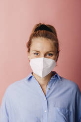 Mid adult businesswoman wearing protective face mask staring while standing against colored background - DAWF01789