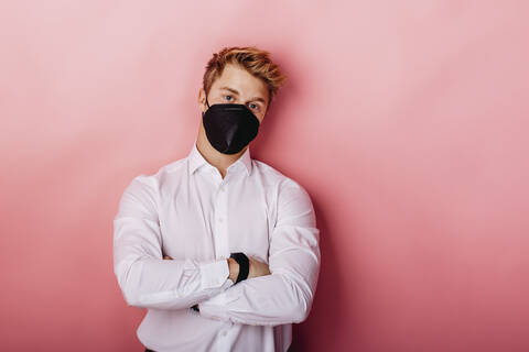 Young businessman wearing FFP2 protective face mask standing with arms crossed against colored background stock photo