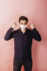 Männlicher Unternehmer mit Gesichtsschutzmaske vor einem farbigen Hintergrund - DAWF01798