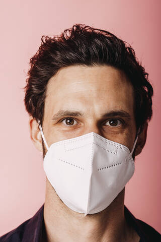 Businessman wearing protective face mask staring while standing against colored background stock photo