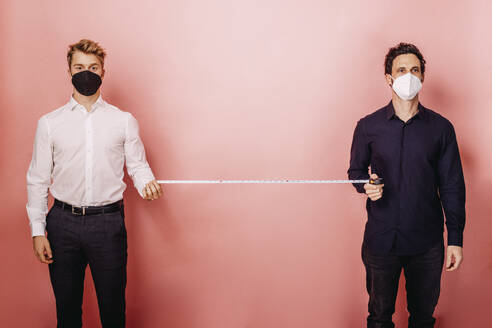 Geschäftsleute messen die soziale Distanz mit einem Maßband, während sie vor einem farbigen Hintergrund stehen - DAWF01808