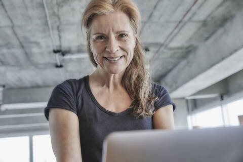 Smiling mature woman with laptop in loft apartment at home stock photo