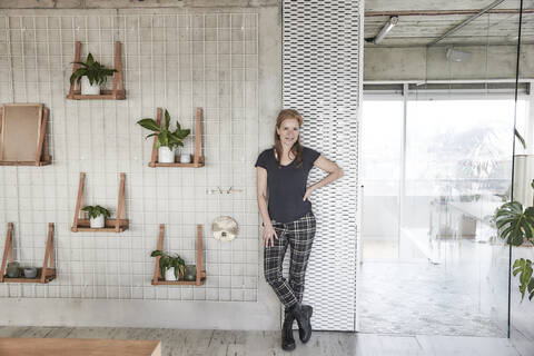 Frau mit Hand auf der Hüfte, die zu Hause an der Wand steht, lizenzfreies Stockfoto