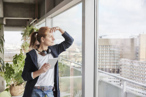 Woman with headphones holding digital tablet while looking through window stock photo