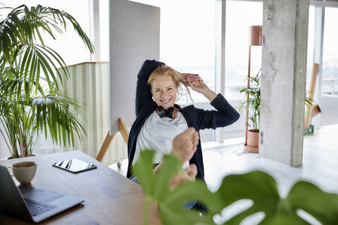 Smiling female entrepreneur with hands behind head relaxing on chair at desk in home office stock photo