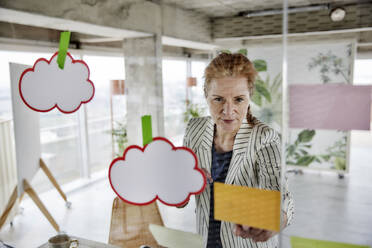 Unternehmerin durch Glas gesehen, während sie im Büro Haftnotizen an die Wand klebt - FMKF07018