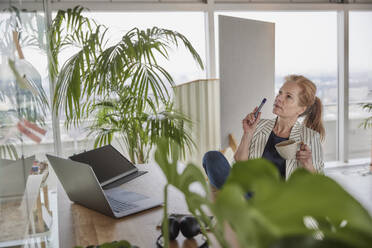 Geschäftsfrau hält Kaffeetasse, während sie einen Geschäftsplan am Schreibtisch im Büro erstellt - FMKF07021
