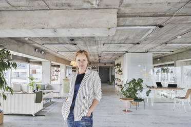 Confident businesswoman with hands in pockets standing in apartment - FMKF07027