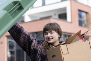 Junge Frau legt Karton in Mülltonne - SGF02762