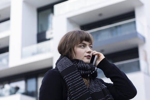Young woman wearing scarf talking on mobile phone while standing against building stock photo