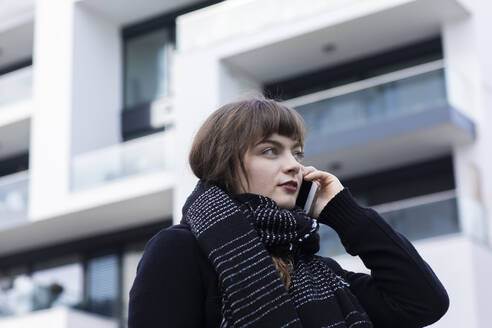 Young woman wearing scarf talking on mobile phone while standing against building - SGF02765