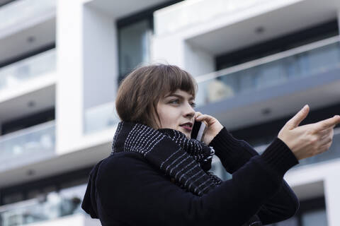 Woman gesturing while talking on mobile phone standing against building stock photo