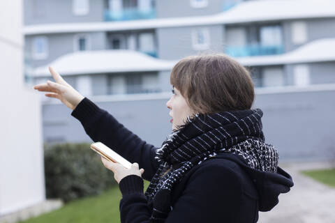 Young woman pointing while using mobile phone standing on street stock photo