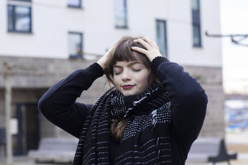 Woman standing with eyes closed and head in hands on street - SGF02768