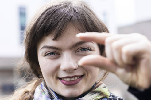 Smiling woman gesturing small hand sign while standing outdoors - SGF02774