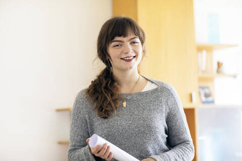 Lächelnde Frau mit Papier in der Hand im Büro stehend, lizenzfreies Stockfoto