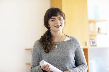 Lächelnde Frau mit Papier in der Hand im Büro stehend - SGF02777
