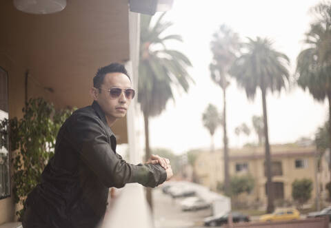 Fashionable man wearing sunglasses looking away while leaning on railing stock photo