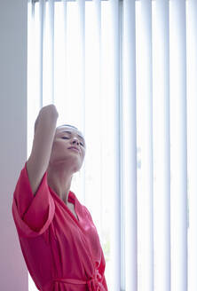 Frau streckt die Hände aus, während sie zu Hause am Fenster steht - AJOF01097