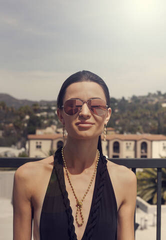Junge Frau mit Sonnenbrille und Badebekleidung lächelt, während sie im Freien steht, lizenzfreies Stockfoto