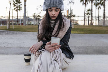 Schönes Teenager-Mädchen, das ein Smartphone benutzt, während es auf einer Bank im Park sitzt - JRVF00283