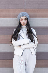 Teenage girl with arms crossed standing while leaning on wall - JRVF00301