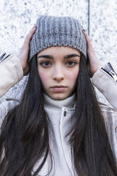 Teenage girl in knit hat with long hair against wall - JRVF00307