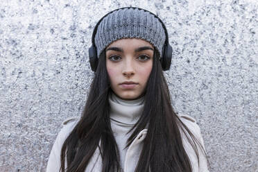 Schönes Teenager-Mädchen mit langen Haaren hört Musik über Kopfhörer gegen silberne Wand - JRVF00311