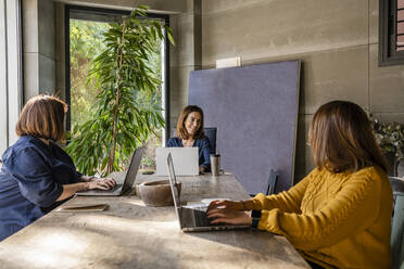 Weibliche Mitarbeiter, die am Konferenztisch im Büro sitzen und diskutieren - DLTSF01625