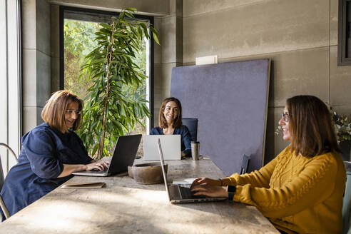 Female colleagues discussing while sitting at conference table in board room - DLTSF01626