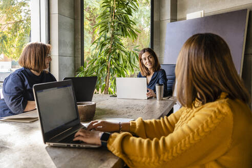 Reife Geschäftsfrau mit weiblichen Kollegen, die am Konferenztisch im Büro sitzen und diskutieren - DLTSF01627