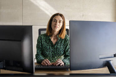 Female entrepreneur with computer sitting at desk in office - DLTSF01638