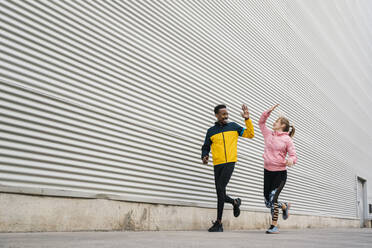 Male and female sportsperson doing high-five while exercising by wall - EGAF01847