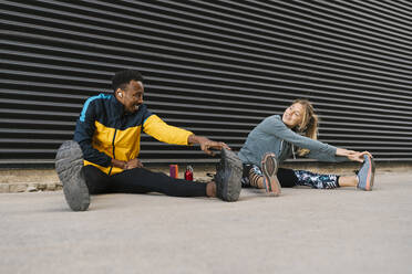 Male and female sportsperson doing stretching exercise while sitting on floor against back wall - EGAF01858