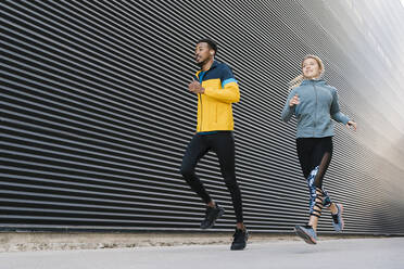 Male and female athlete running on sidewalk during sports training by wall - EGAF01864