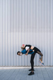 Playful man lifting woman on back by wall during COVID-19 - EGAF01875