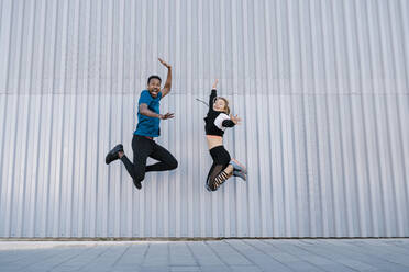 Carefree male and female friends jumping high by wall - EGAF01876