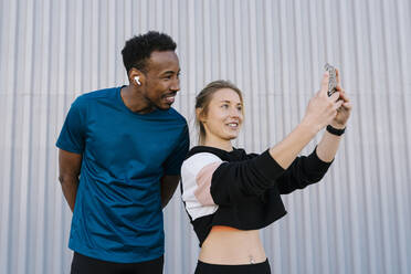 Weibliche Athletin mit Mann, der ein Selfie mit dem Handy macht, während er an der Wand steht - EGAF01882