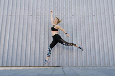 Carefree female athlete jumping by wall during sports training - EGAF01893