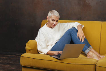 Ältere Frau benutzt einen Laptop, während sie auf dem Sofa im Wohnzimmer sitzt - OIPF00374
