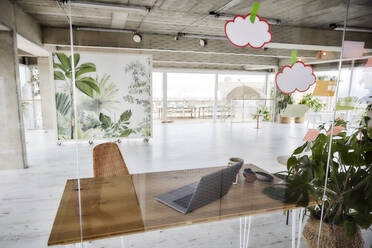 Laptop on wooden table in empty apartment seen through glass wall - FMKF07031