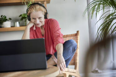 Woman with headphones doing video call on laptop at home - FMKF07037