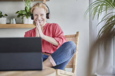 Lächelnde Frau grüßt während eines Videoanrufs auf dem Laptop zu Hause - FMKF07038