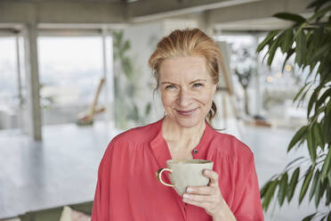Lächelnde reife Frau hält Kaffeetasse zu Hause - FMKF07043