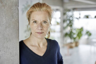 Woman with hazel eyes leaning on wall at home - FMKF07050