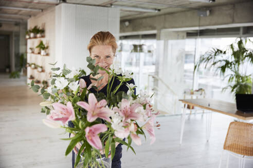 Smiling woman with bunch of flowers at home - FMKF07053