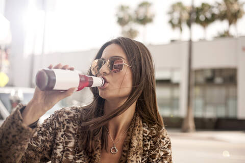 Schöne Frau mit Sonnenbrille trinkt aus einer Flasche in der Stadt, lizenzfreies Stockfoto